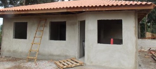 Casa com cobertura de telha e todas as paredes rebocadas.